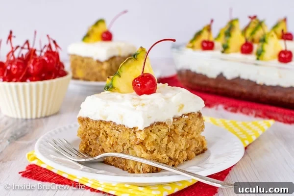 A white plate with a square of homemade pineapple cake topped with pineapple frosting and cherries