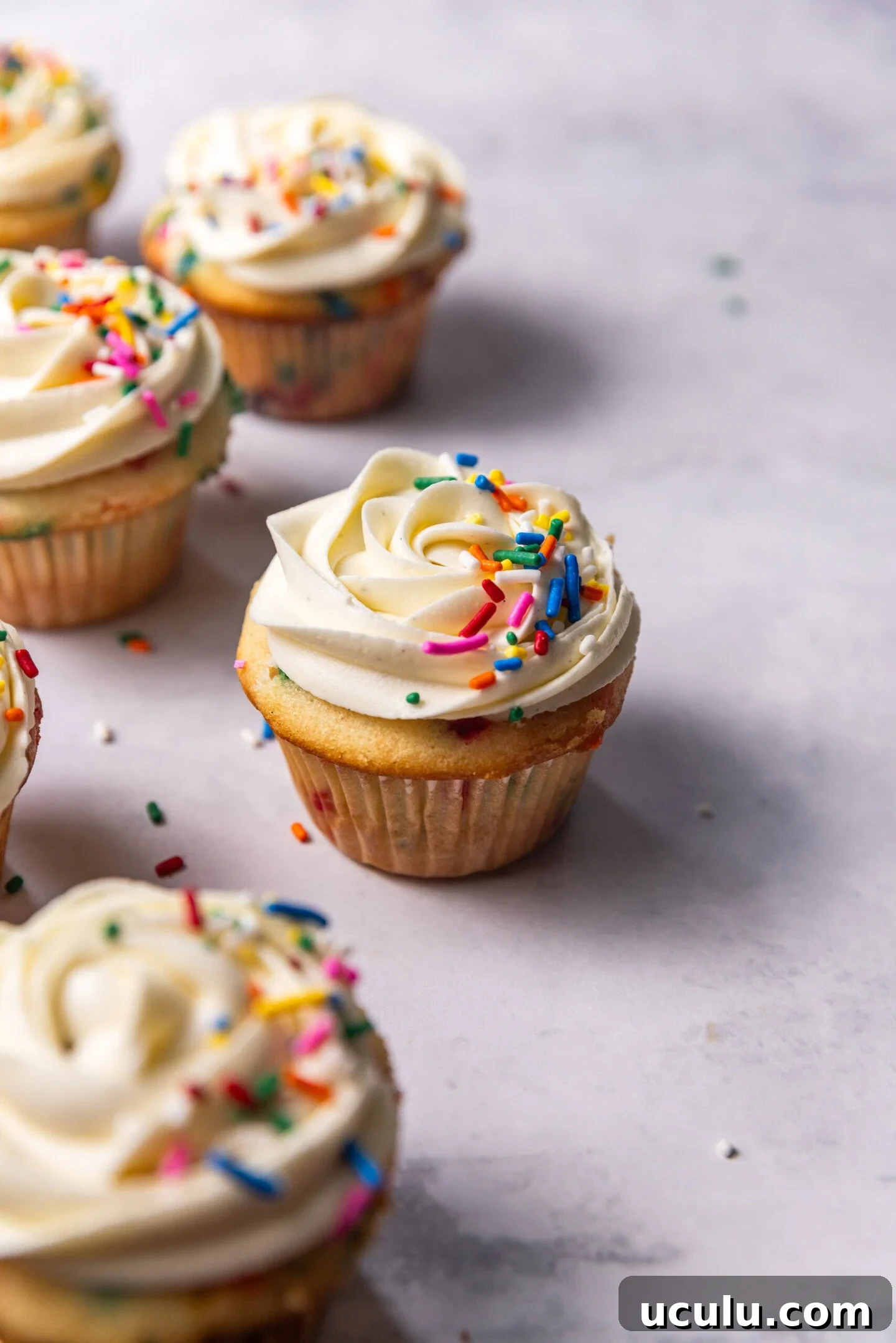 Six Moist Small Batch Funfetti Cupcakes with double vanilla buttercream piped on top and rainbow sprinkles sprinkled on.