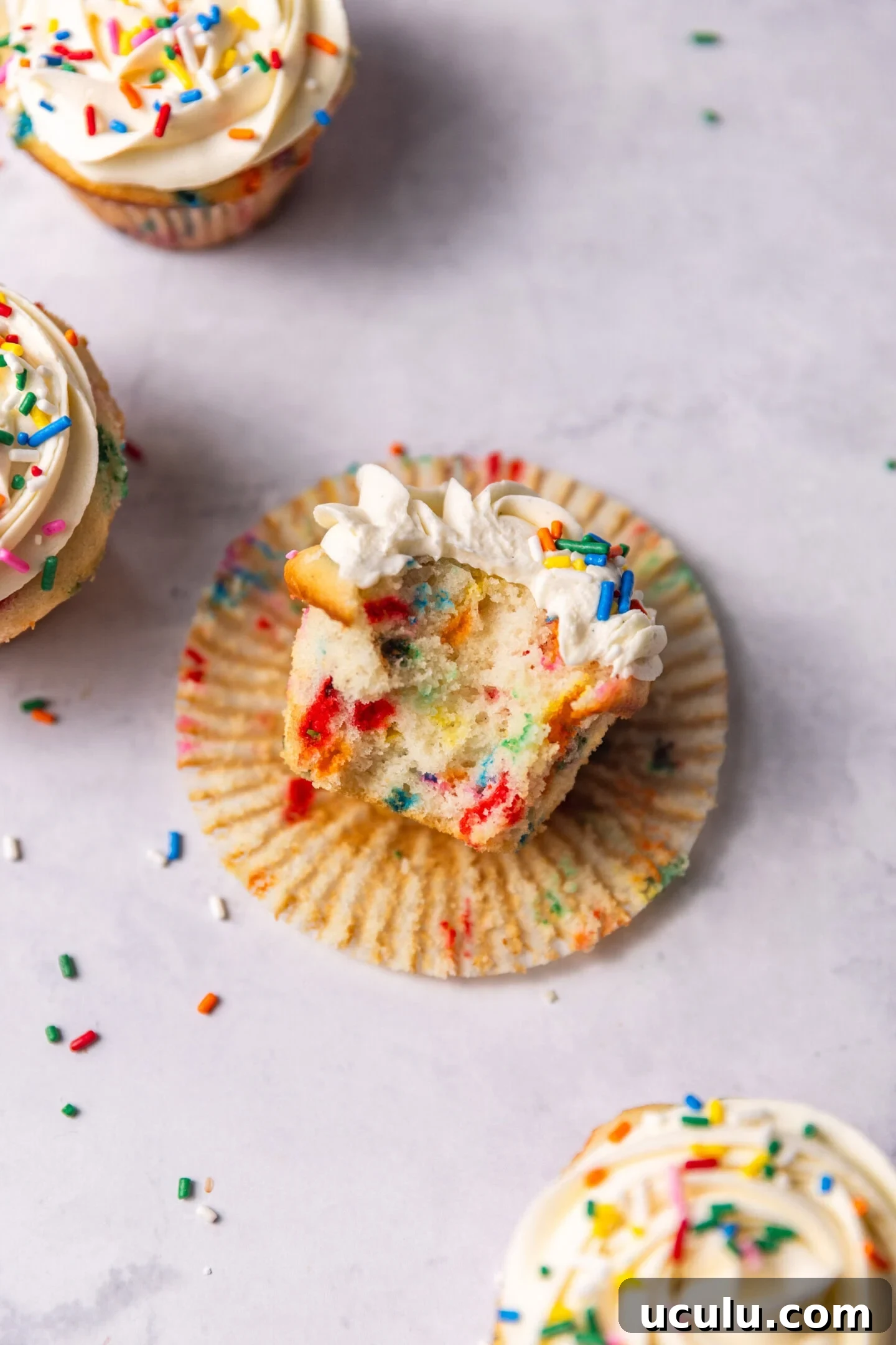 Close up of funfetti cupcake with a bite missing showing off soft and fluffy texture and pops of color from rainbow sprinkles.