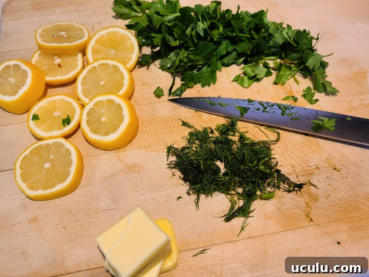 Cut butter slices, lemon slices, and fresh minced parsley and dill on a cutting board with a knife 