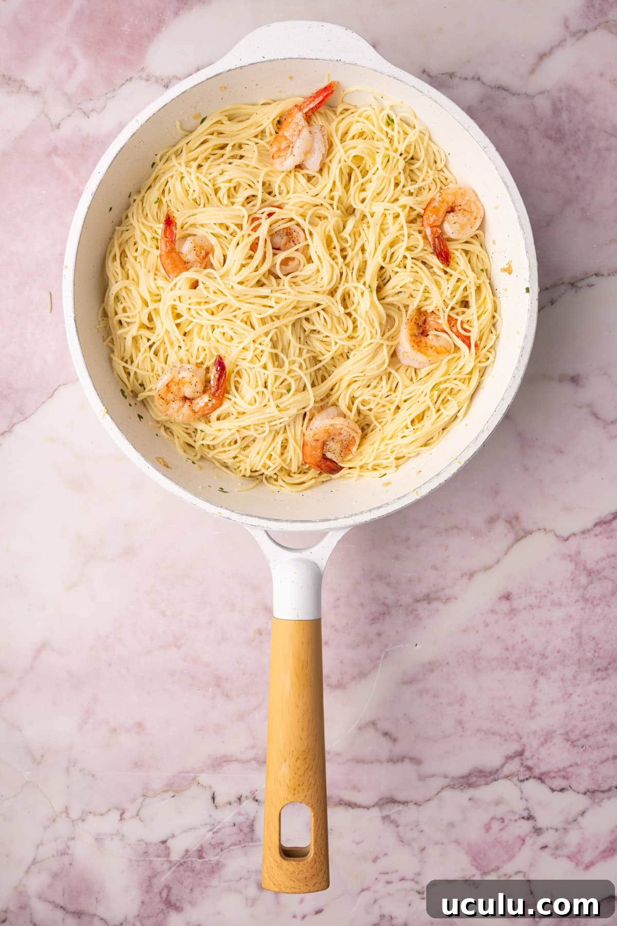 Adding cooked shrimp back to pasta tossed with lemon juice and zest, garlic, and Parmesan cheese. 