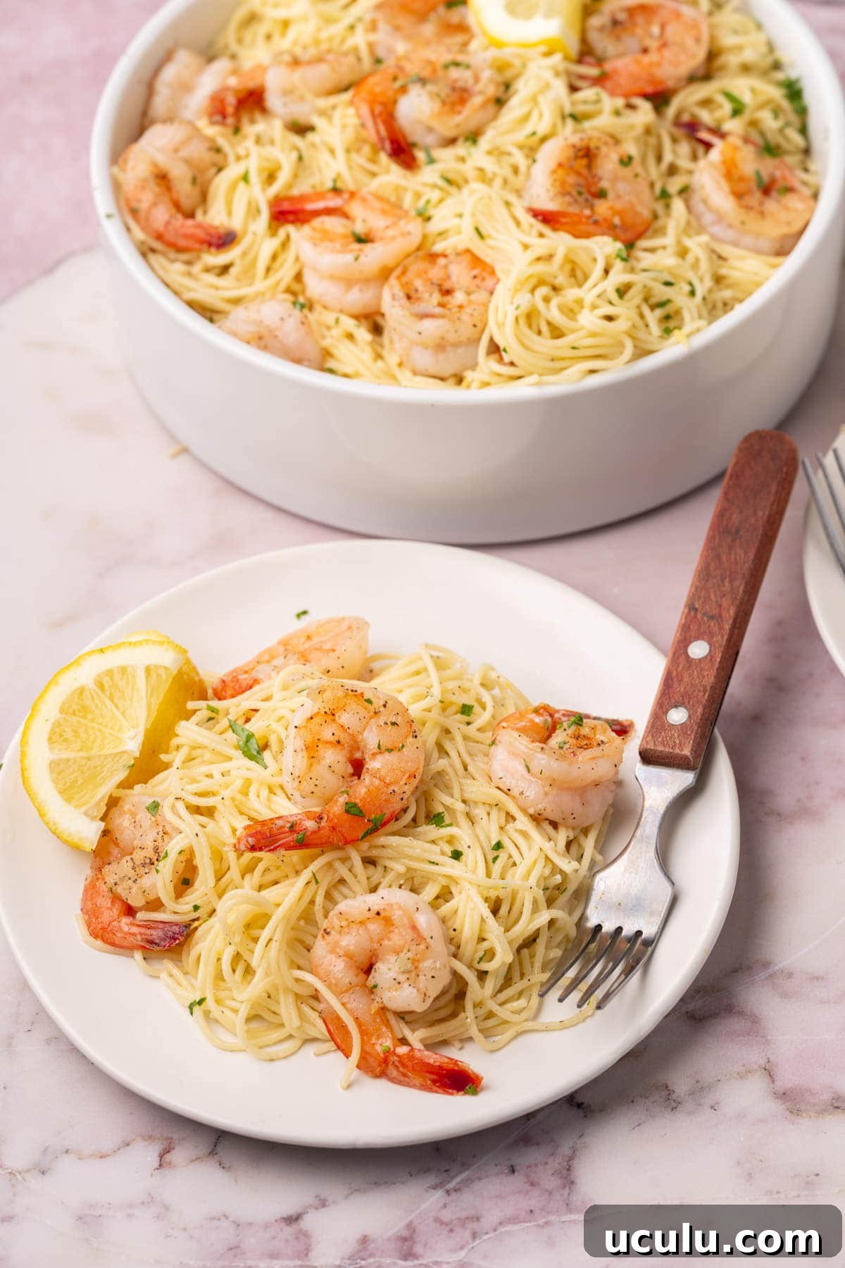 Lemon shrimp pasta served on a plate with a fork, with the serving bowl in the background. 