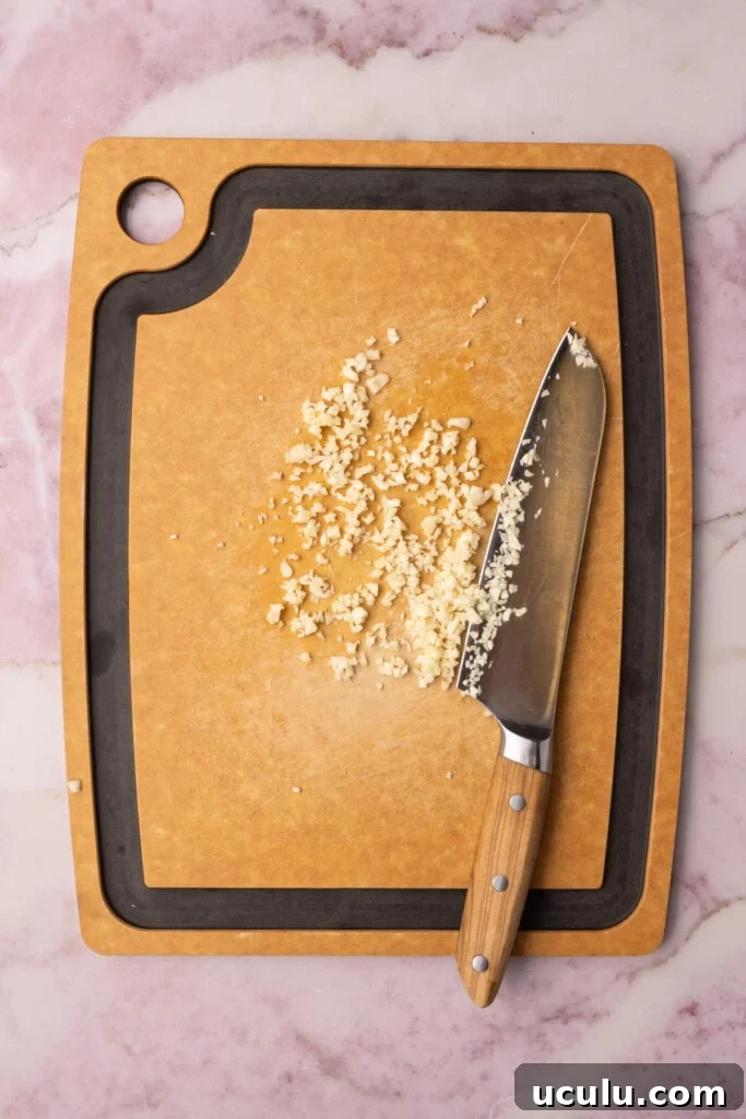 Minced garlic on a chopping board next to a sharp knife. 