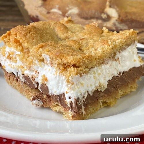 Layers of thick chocolate bars and marshmallow creme between graham cracker layers in a big square piece of the best smores cake