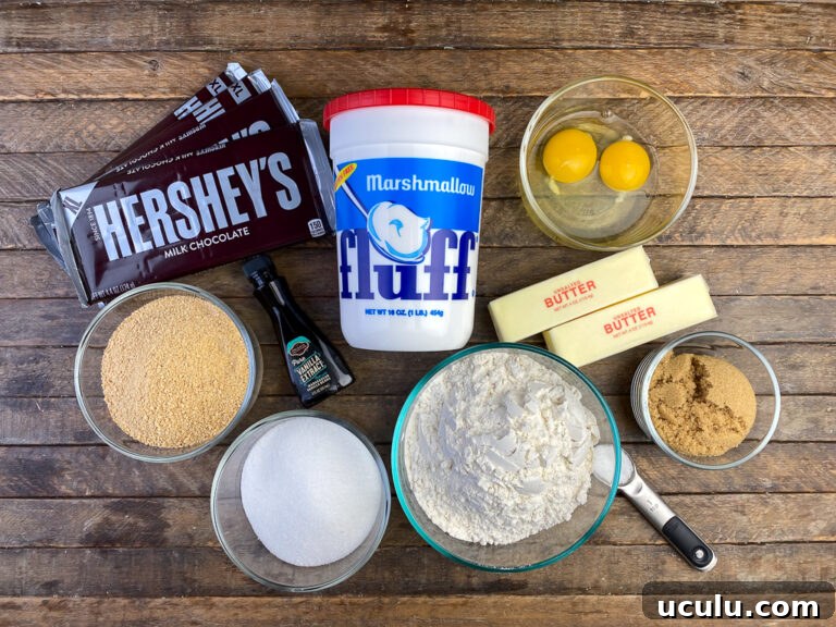 Ingredients to make smores cake on a brown wooden counter top are Hersheys milk chocolate bars, marshmallow fluff, eggs, butter, brown sugar, salt, flour, sugar, vanilla and graham cracker crumbs