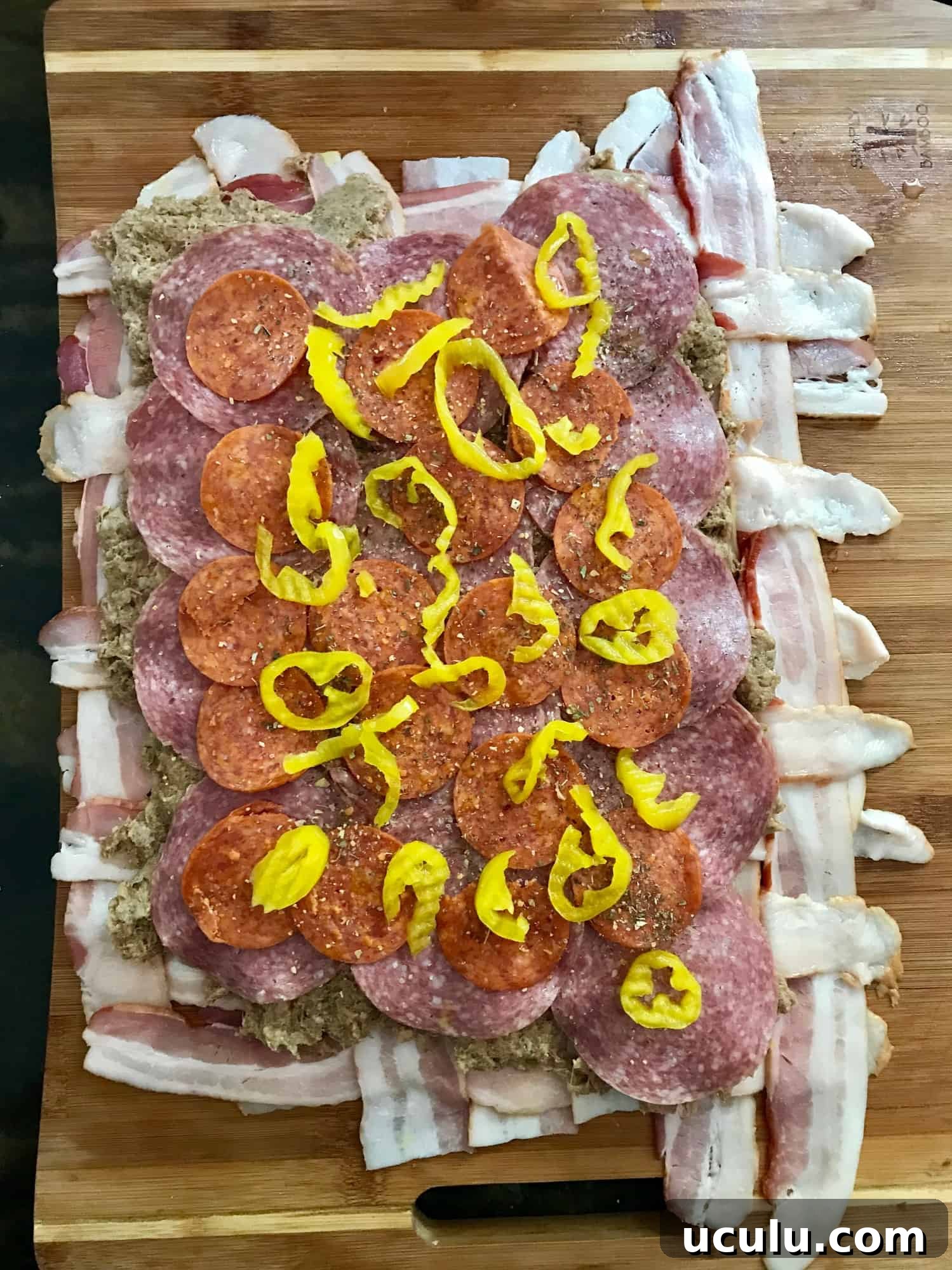 Bacon weave topped with meat and peppers on wooden cutting board overhead shot