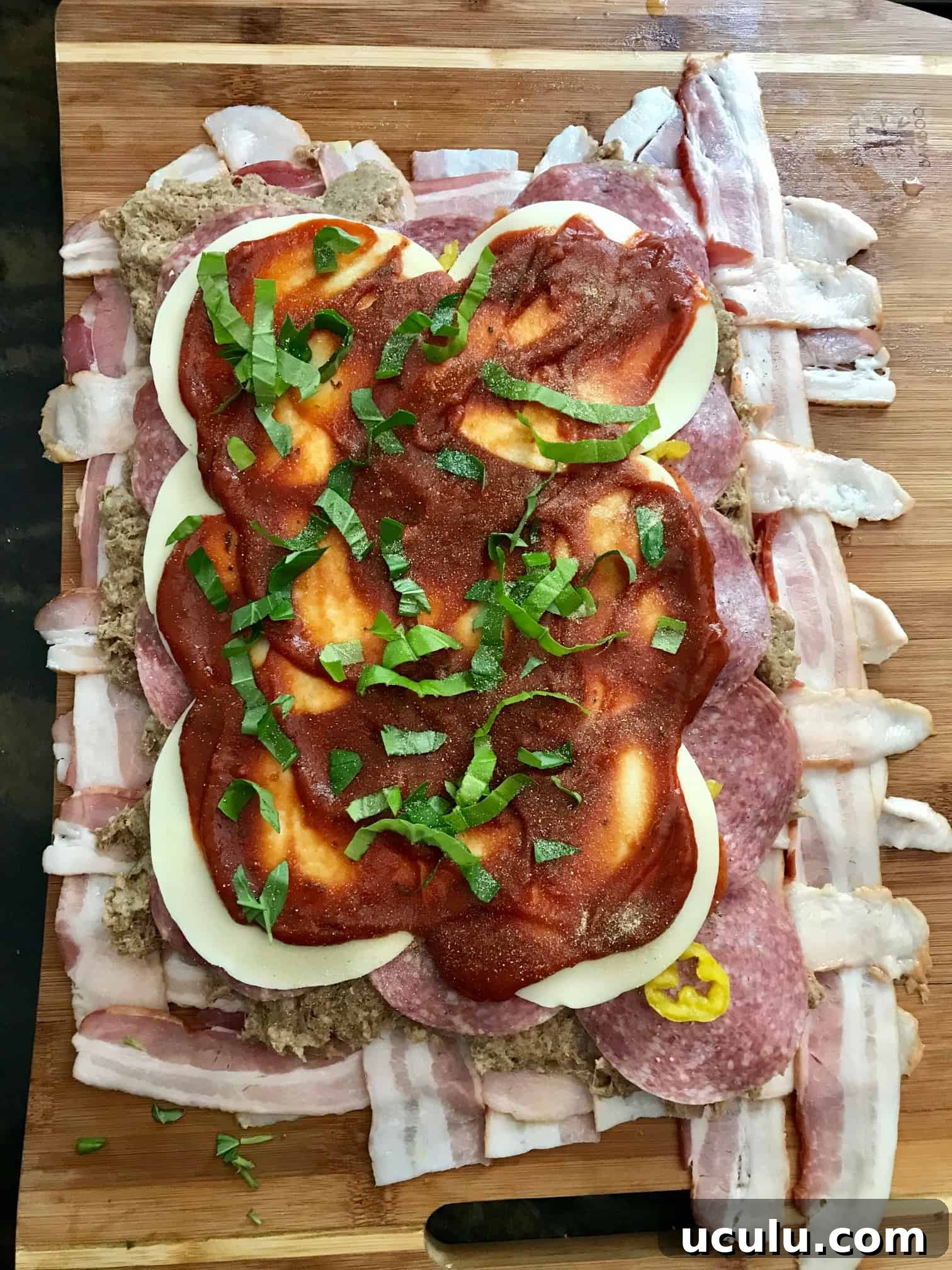 Bacon weave topped with cheese and sauce on wooden cutting board overhead shot