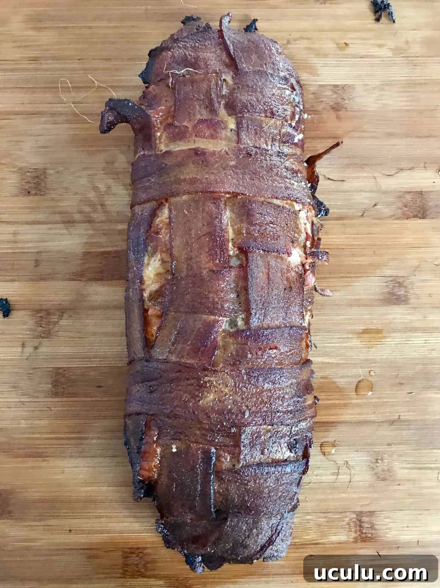 Pizza Bacon Explosion smoked sitting on wooden cutting board overhead shot