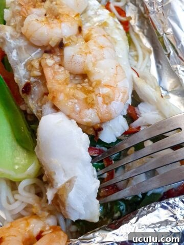 Close up of a piece of cooked fish on a pork held above a dish of cod and prawn fish parcels.