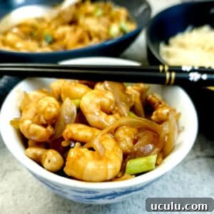 A shall bowl filled with kung pao prawns with a pair of chopsticks balanced on top.