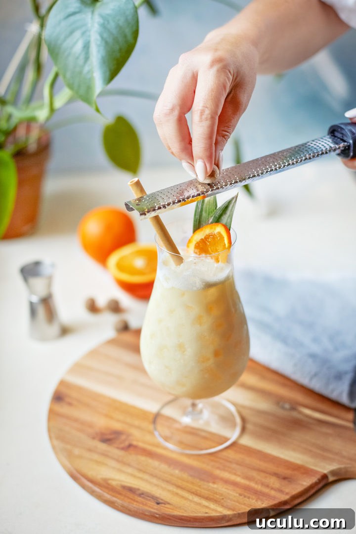 woman garnishing a painkiller recipe with fresh nutmeg