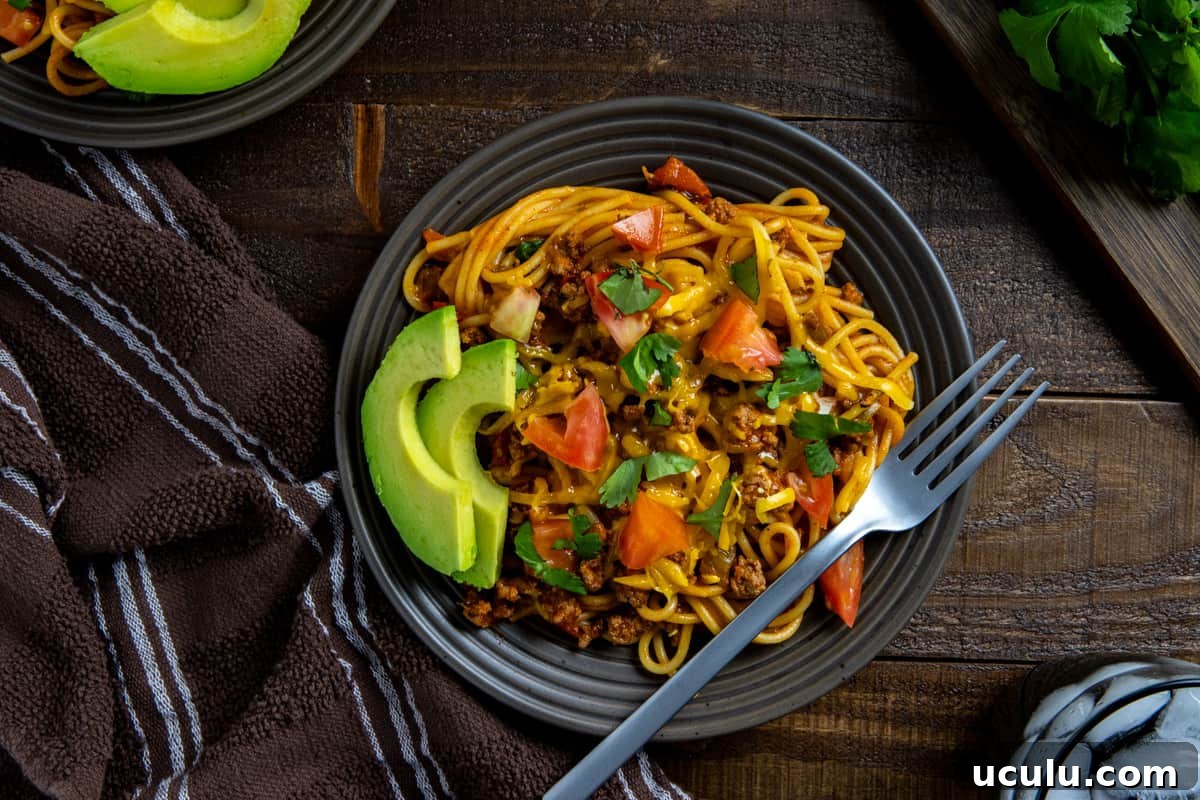 Plated spaghetti on brown plate with avocado slices and a fork on the side.