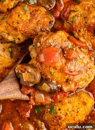 Spatula lifting a chicken thigh from pan of chicken cacciatore.