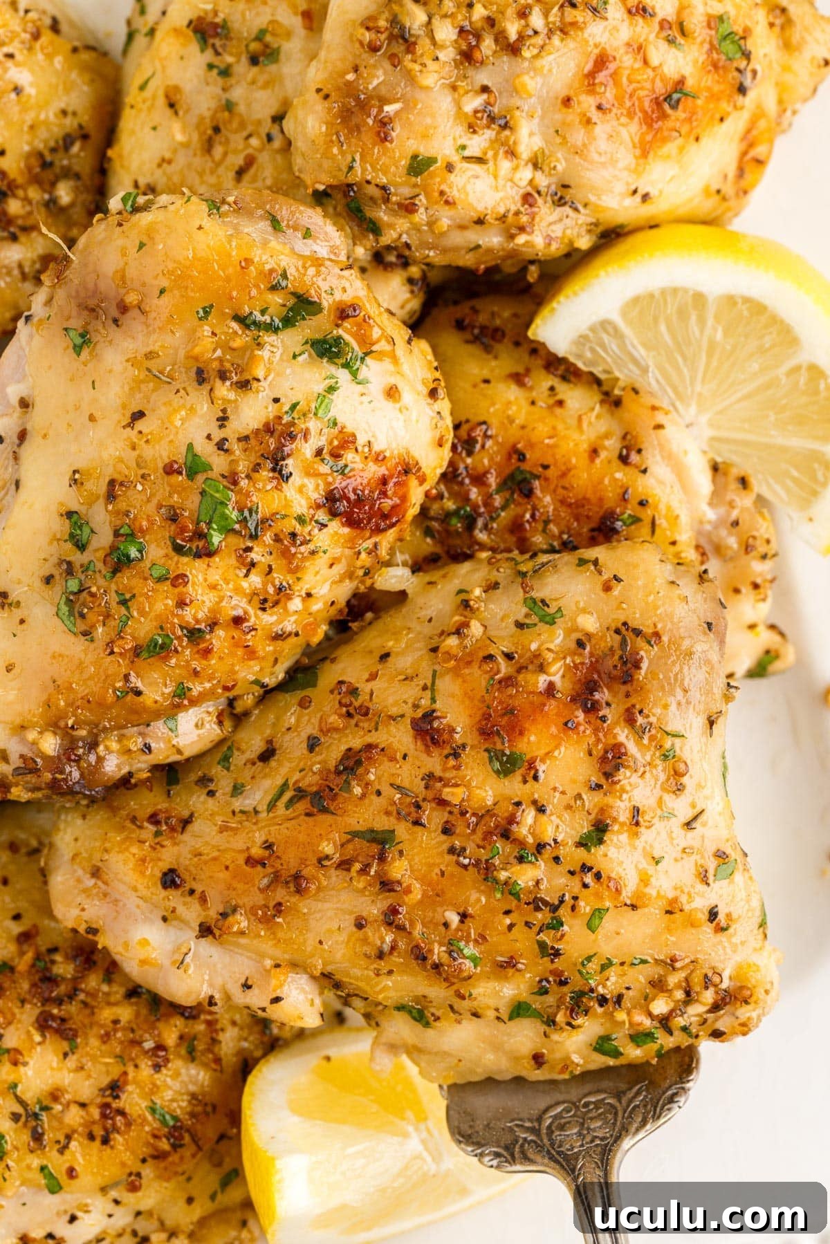 Baked Chicken Thighs on a plate with lemon slices.