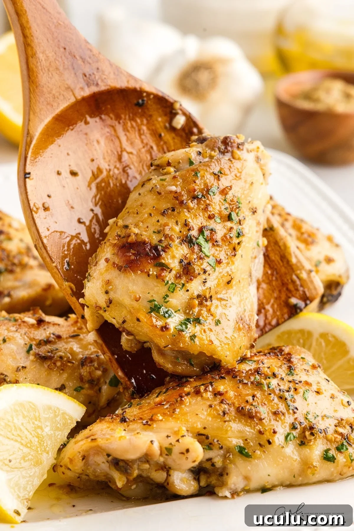 A Baked Chicken Thigh on a wooden spoon and some on a platter.