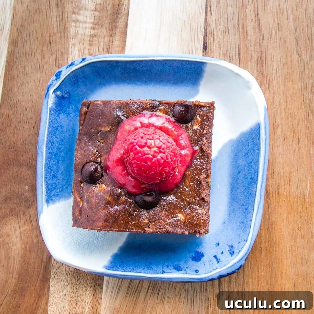 brownie on a bright blue plate with raspberry sauce on top. 
