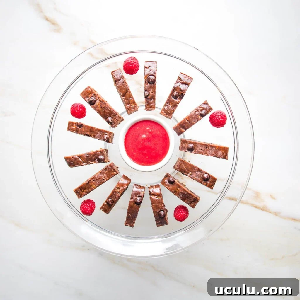 Thinly sliced brownies place in a circle around a bowl of raspberry sauce. 