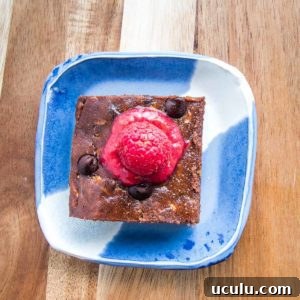 brownie on a bright blue plate with raspberry sauce on top.