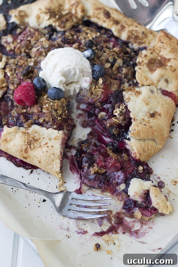 a slice taken out of the galette showing the juicy berry filling with a fork beside it and a dollop of ice cream on top