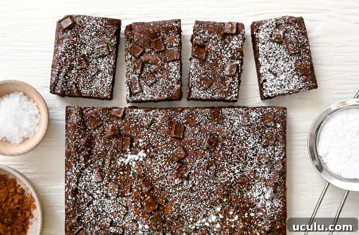 Fudgy homemade brownies dusted with powdered sugar next to a sifter containing powdered sugar.