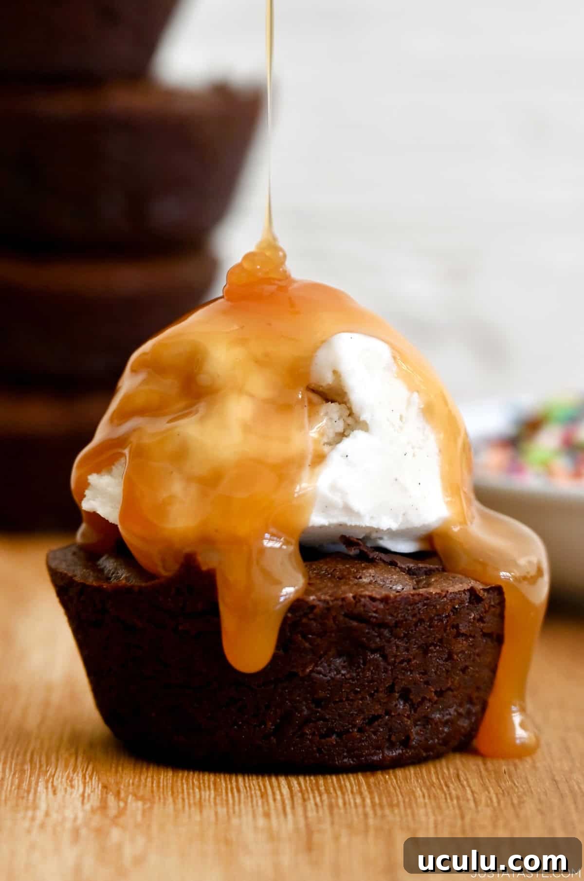 A fudge brownie cupcake topped with vanilla ice cream and a drizzle of caramel sauce.