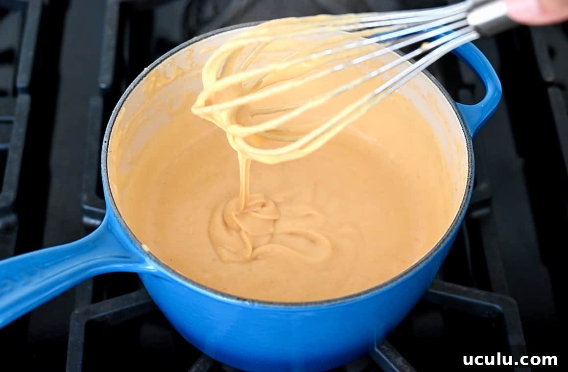 Melted cheese in a blue saucepot with a whisk