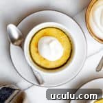 A lemon pudding cake on a plate dolloped with whipped cream.