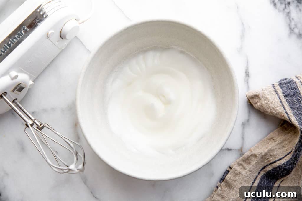 Process shot showing egg whites beat to stiff peaks in a stand mixer.