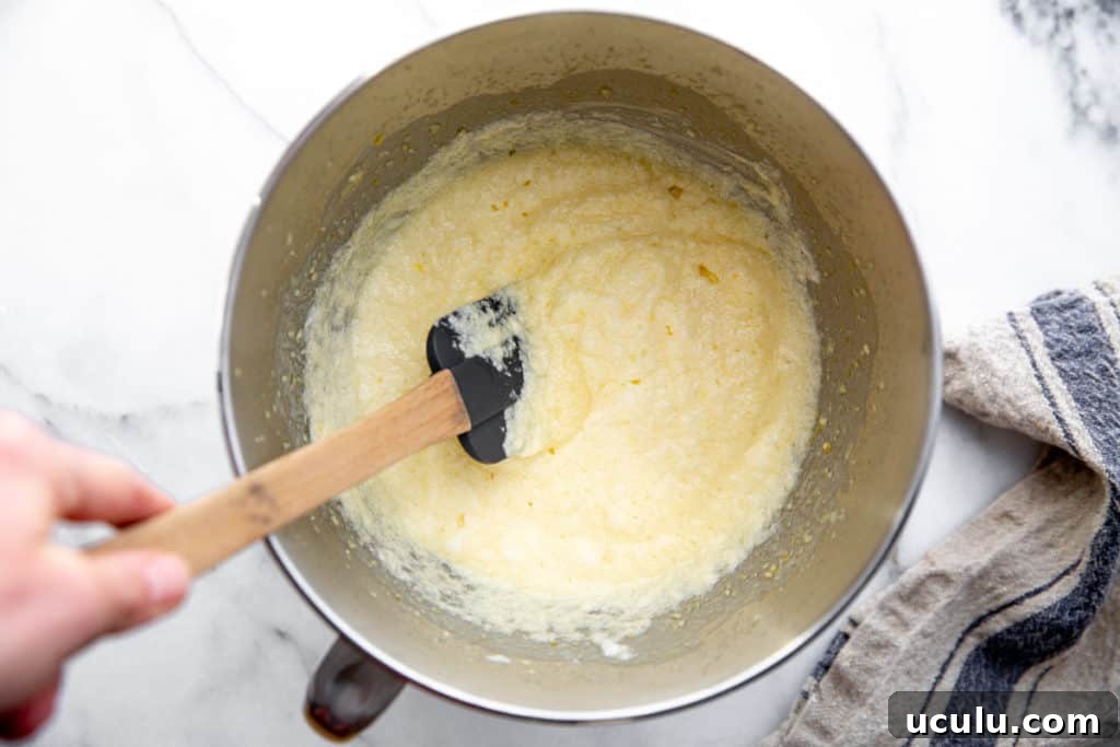 A hand stirring the lemon pudding cake batter in a bowl.