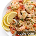 Garlic ginger pan seared shrimp on a white serving plate garnished with lemon slices and chopped parsley.