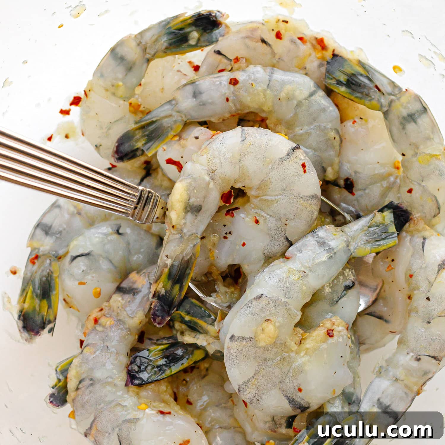 Raw shrimp being mixed together with garlic, ginger, red pepper flakes, salt and pepper.