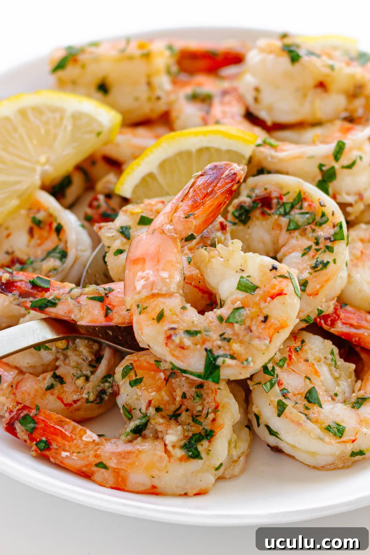 Garlic ginger sautéed shrimp on a white serving plate with serving spoon. 