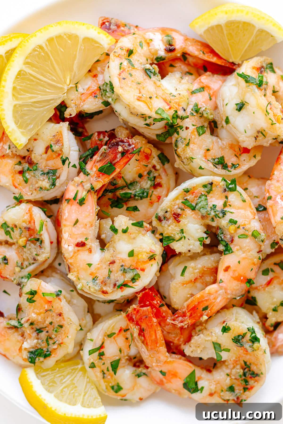 Garlic ginger sautéed shrimp on a white serving dish garnished with lemon slices and chopped parsley. 