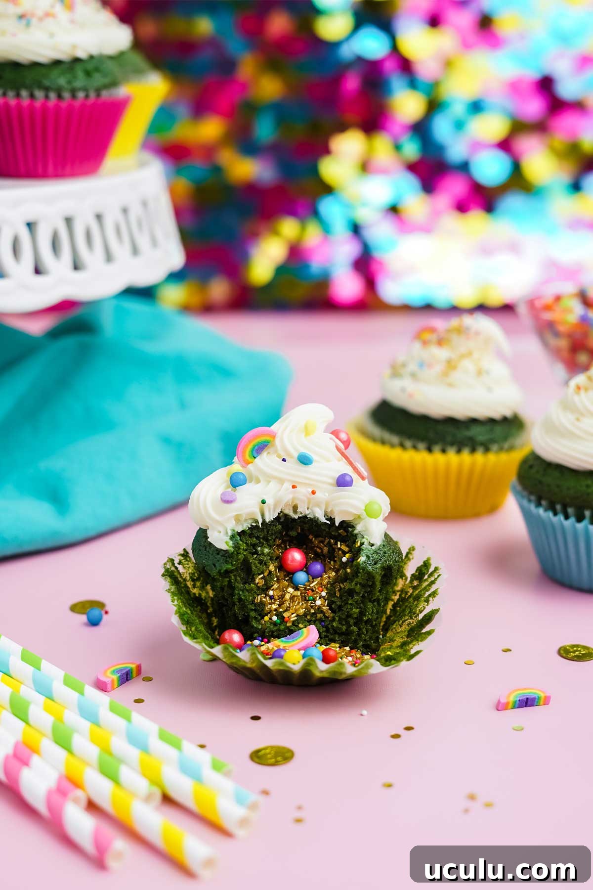 St Patrick's Day cupcake with bite missing and sprinkles in the middle with cake stand in the background.