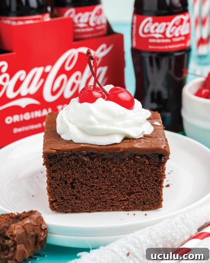 Slice of coca cola cake topped with whipped cream and a cherry.