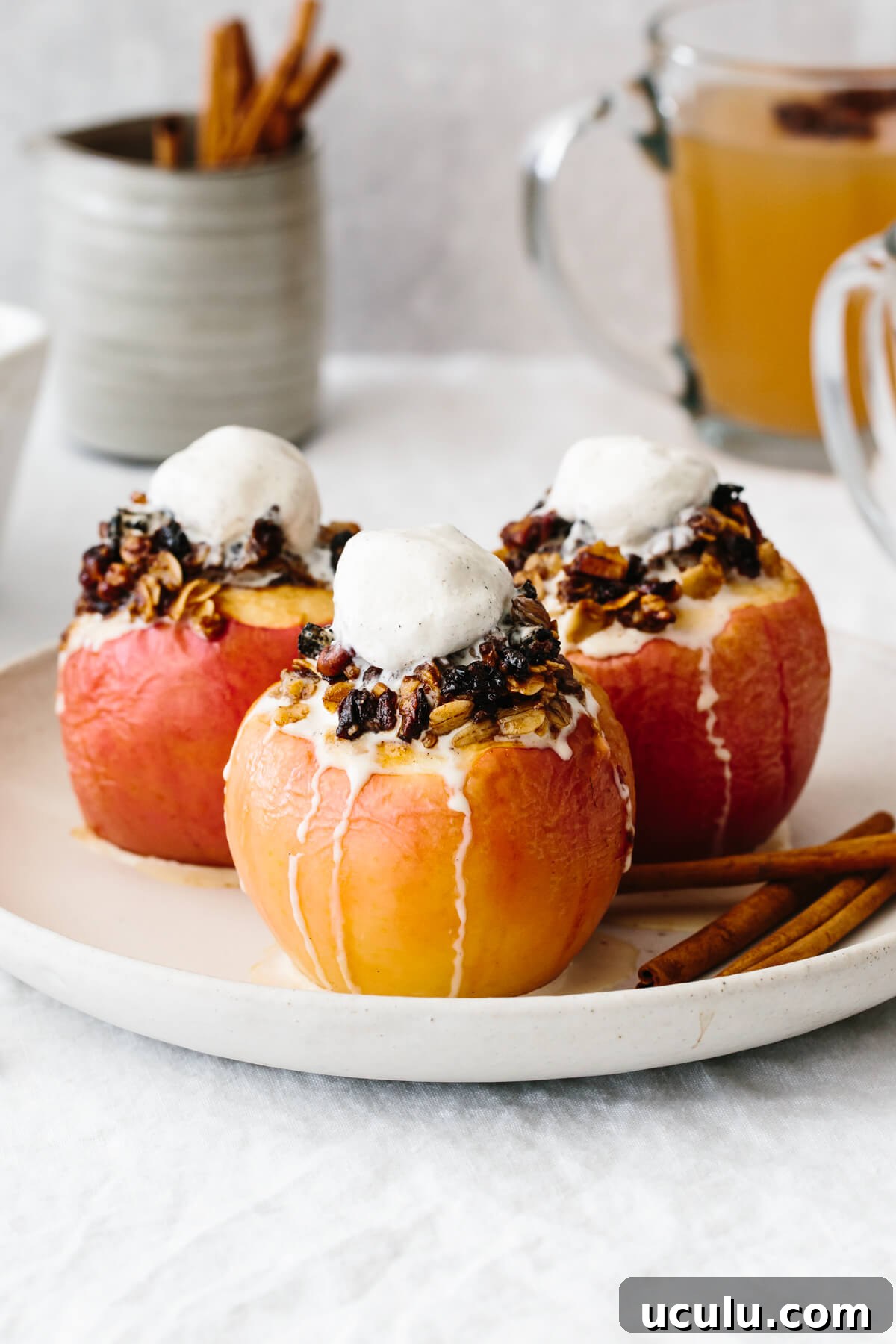 Three baked apples on a plate with melted ice cream on top.