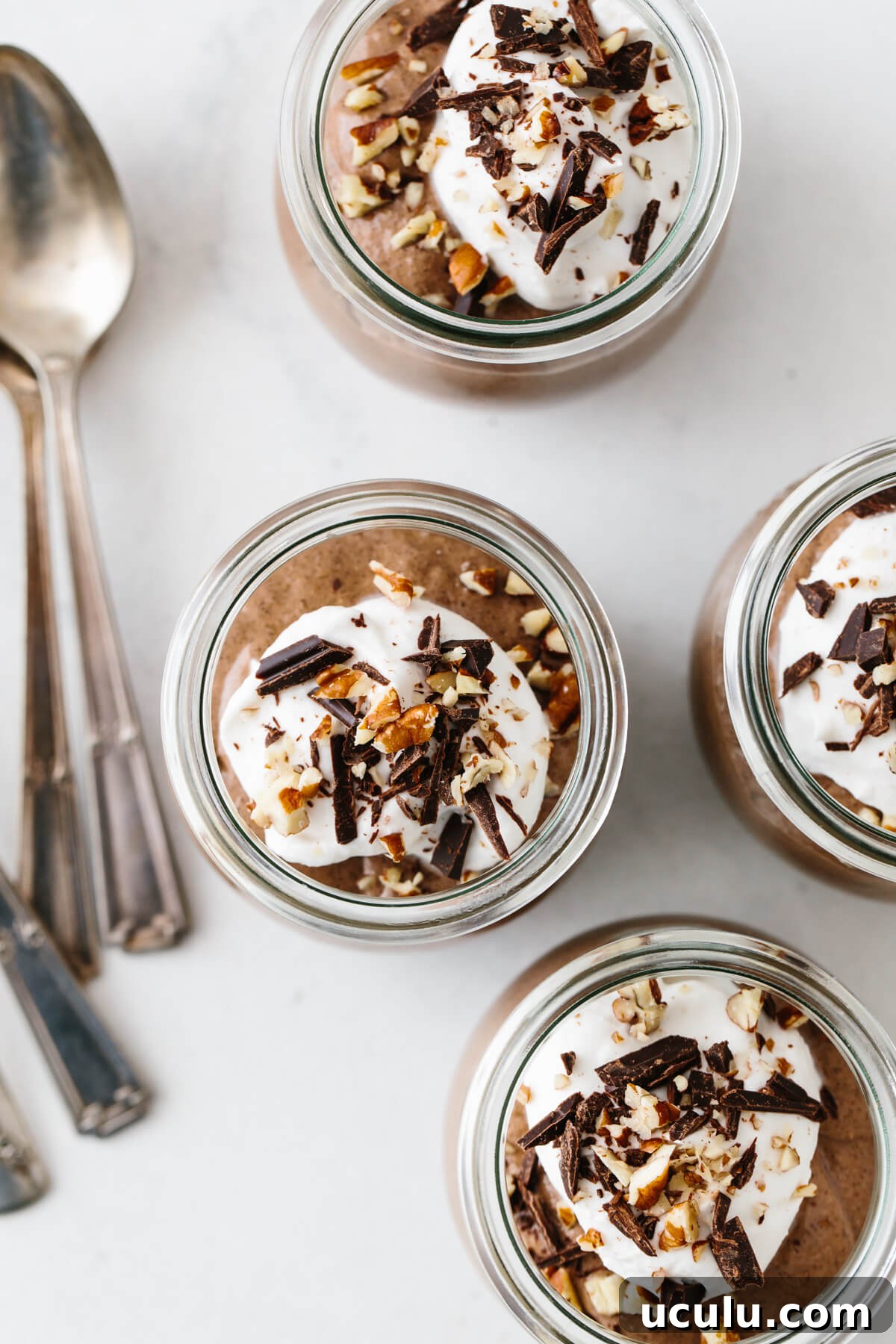 Four servings of chocolate chia mousse topped with coconut whipped cream, nuts and chocolate.