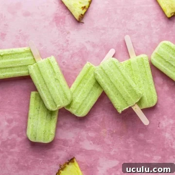 Homemade pineapple coconut popsicles on a pink background.
