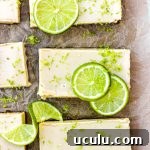 Key lime pie bars with fresh lime slices and lime zest on brown parchment paper.