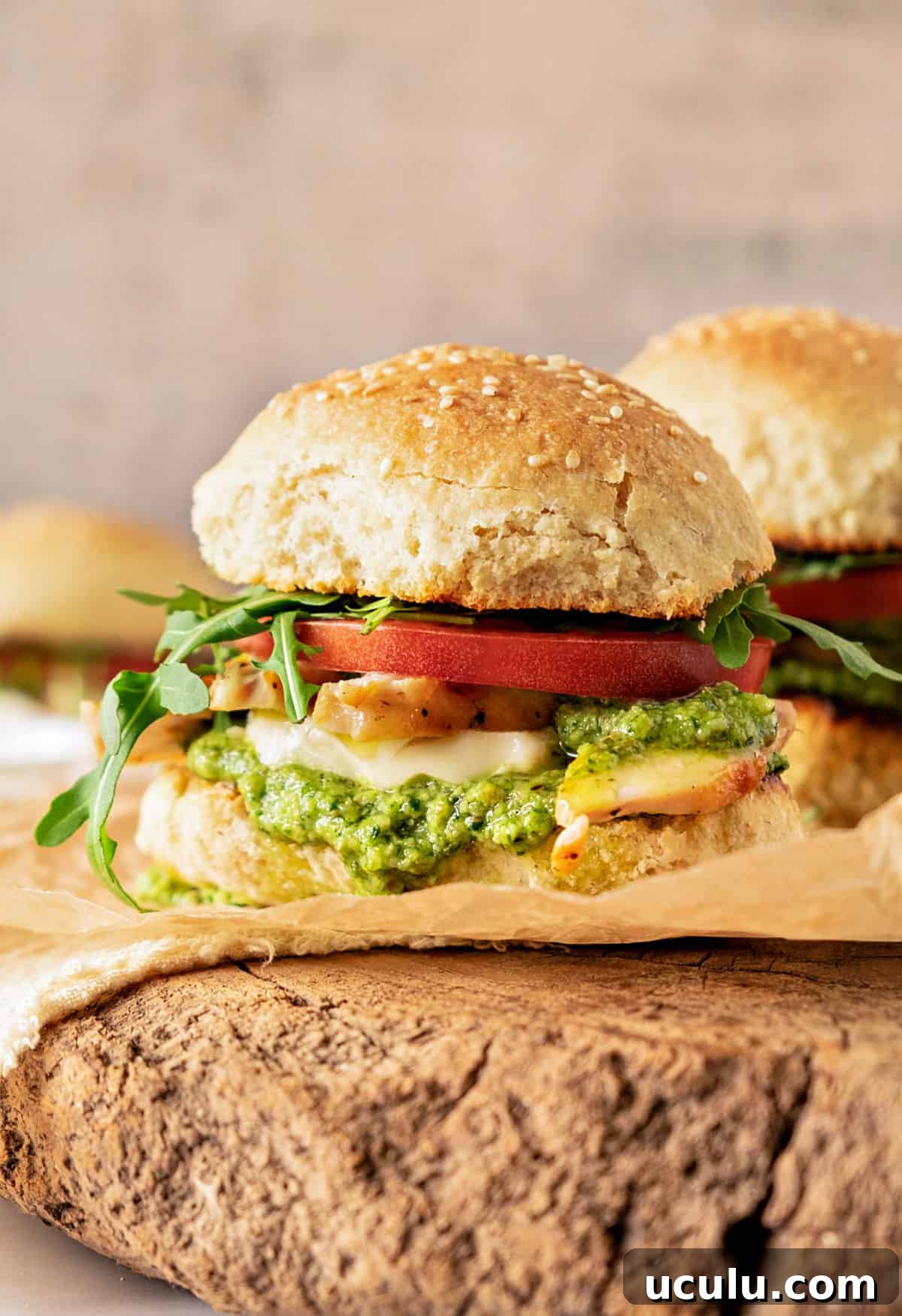 Wooden round with pesto chicken tomato sandwich. Gray background.