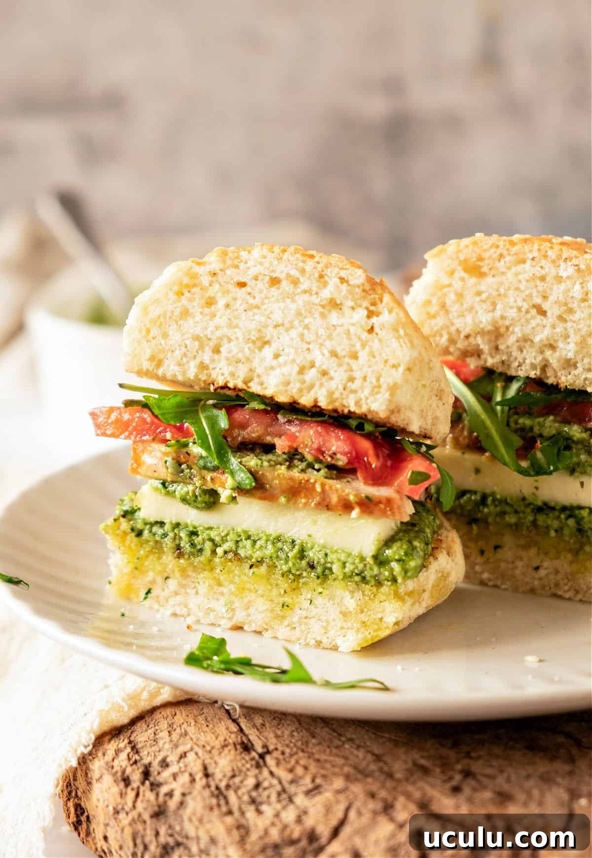 Halved chicken pesto tomato sandwich on a white plate. Gray background.