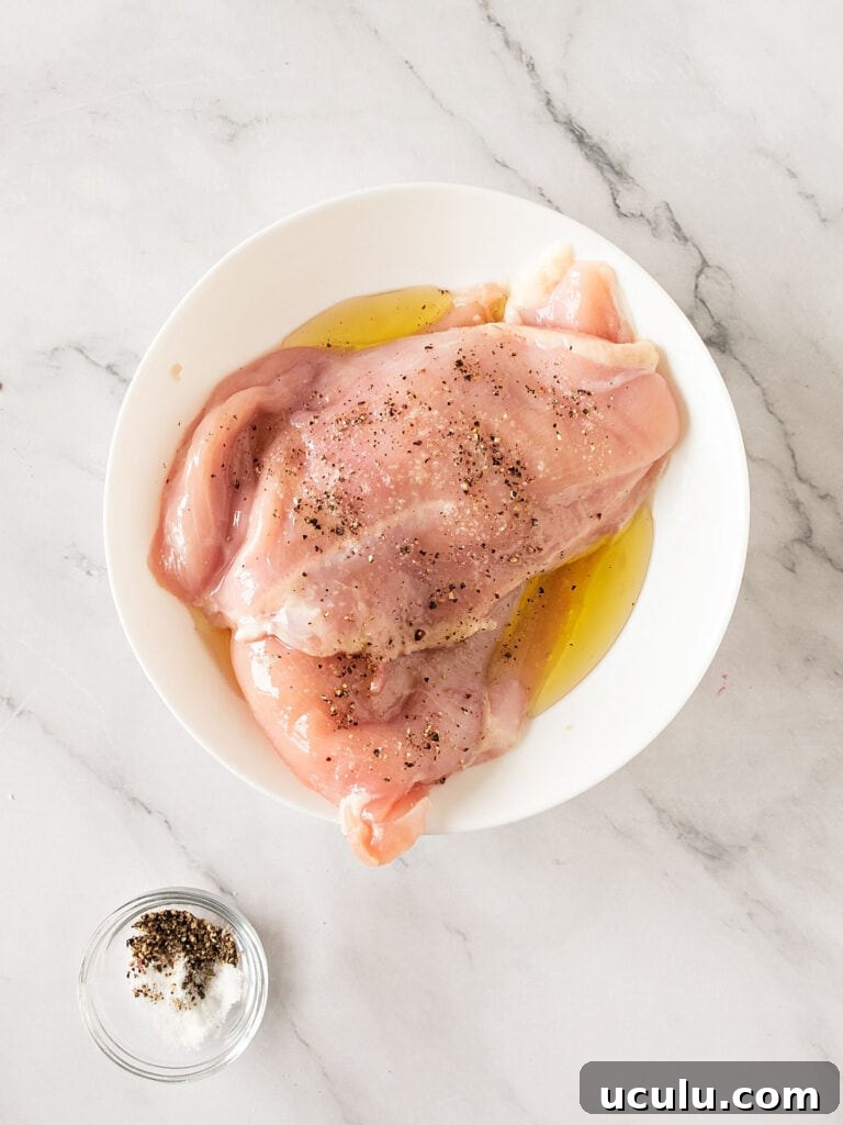 Marinating chicken breasts in a white bowl. White marbled surface.