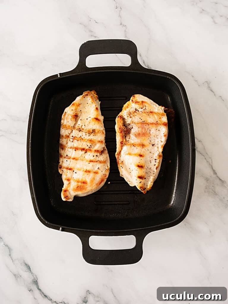 Grilled chicken breasts on a cast iron pan. White marbled surface.