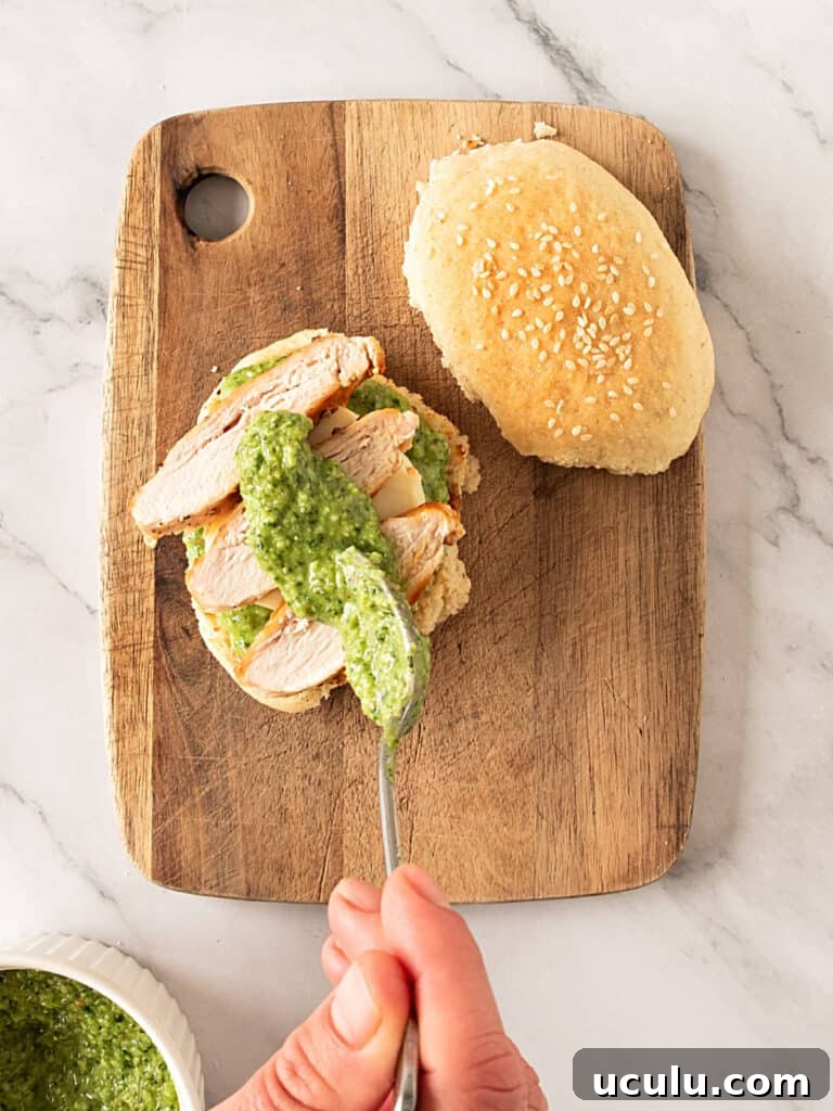 Assembling a chicken pesto sandwich on a wooden board. White marbled surface.