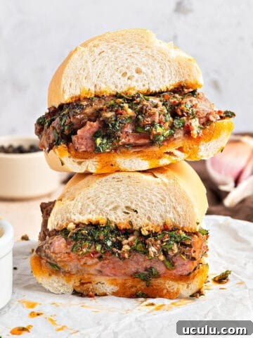 Close up stack of chimichurri steak sandwich on white parchment. Bowls with sauce, light gray background.