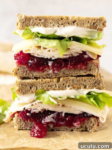 Stack of two halves of turkey cranberry lettuce sandwich on a beige paper.