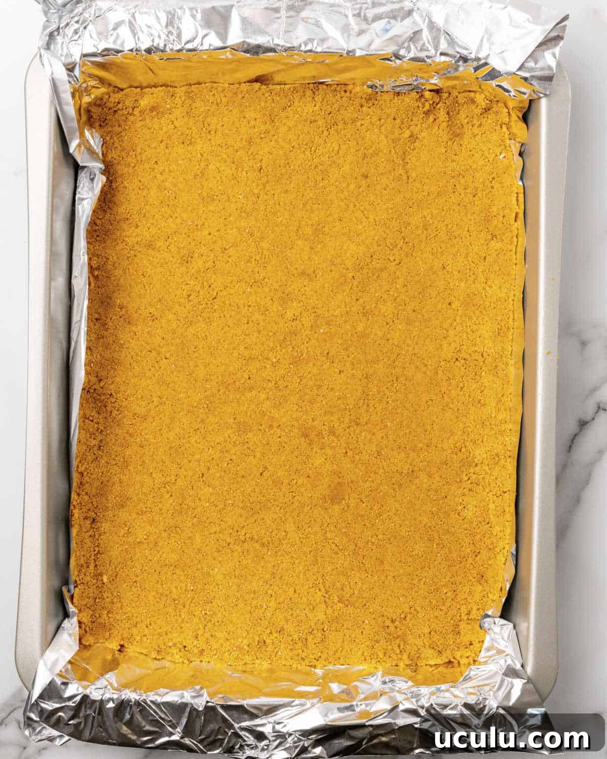 Graham cracker crust pressed on a rectangular pan lined with foil.