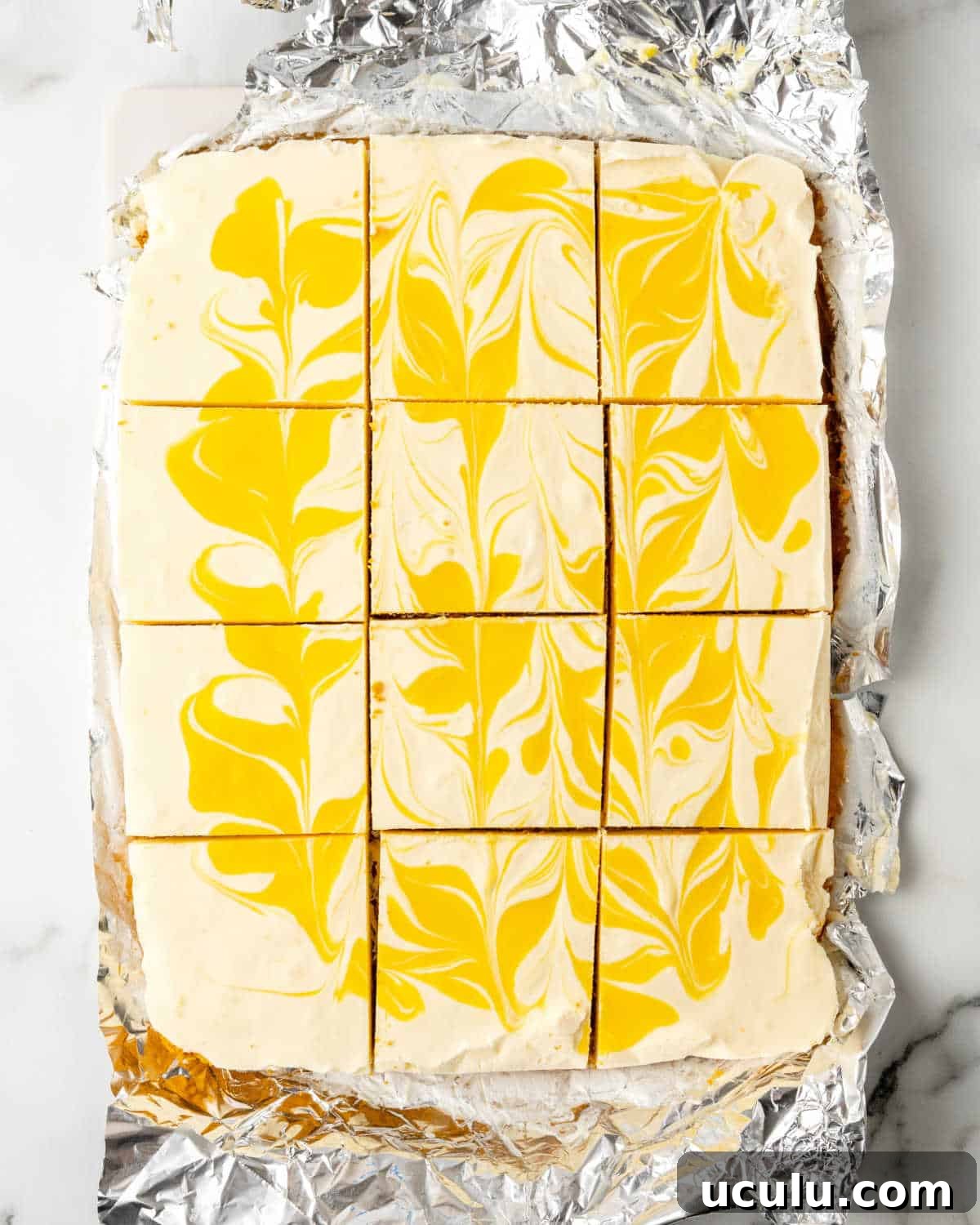 Cut squares of a rectangular passionfruit cheesecake on aluminum paper.