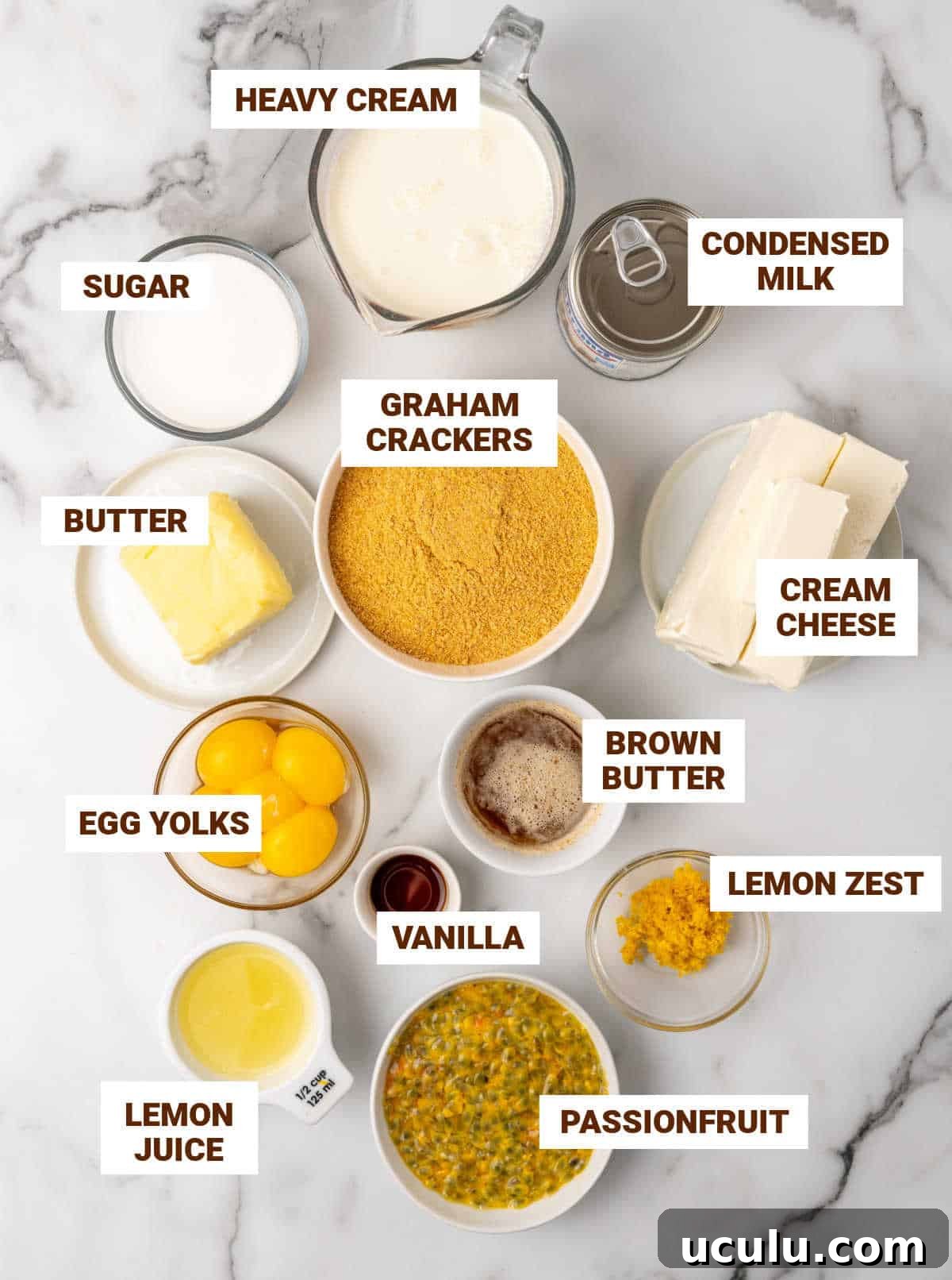 Grey white marble surface with bowls containing ingredients for passionfruit cheesecake including yolks, sugar, condensed milk, butter, lemon, cookie crumbs, cream.