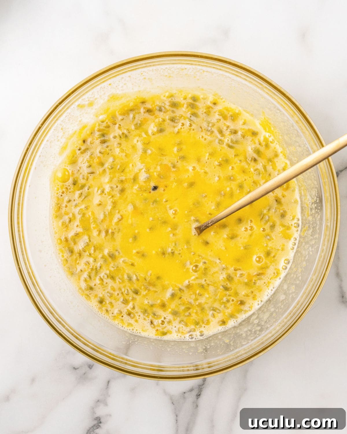 Seeded passion fruit pulp and yolks in a glass bowl. Wooden spoon. White background.